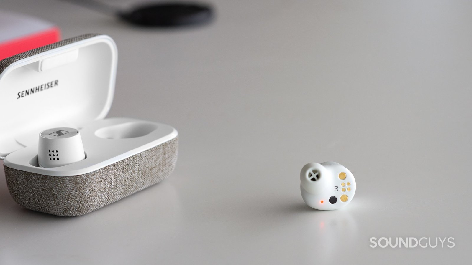 Một chiếc tai nghe Sennheiser Momentum True Wireless 2 nằm ngoài hộp sạc mở, cho thấy thiết kế và cảm biến tự động nhận diện tai.