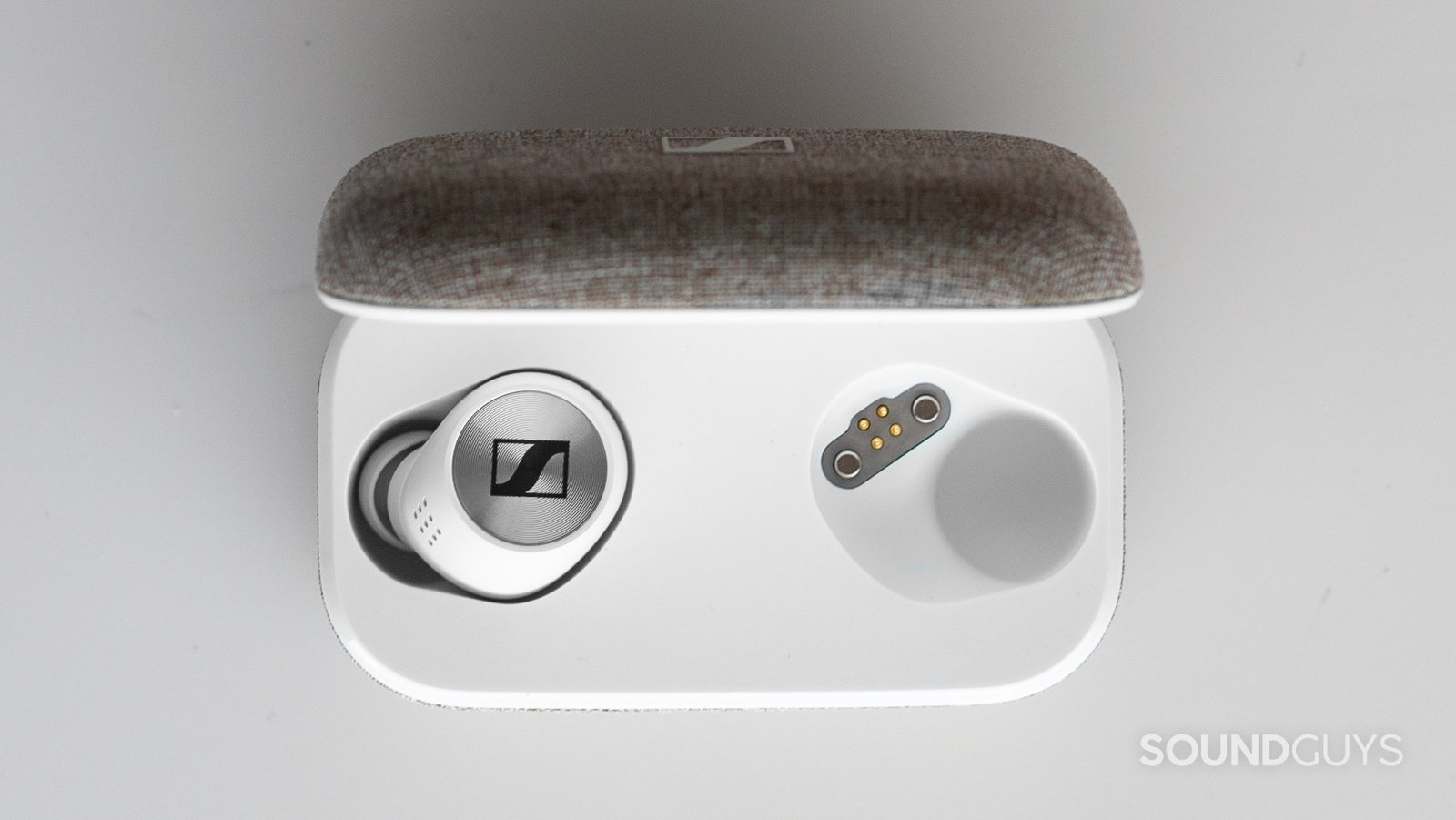 Tai nghe Sennheiser Momentum True Wireless 2 nằm trong hộp sạc trên bàn trắng, cho thấy mặt lưng kim loại chứa điều khiển cảm ứng.