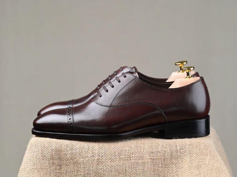 Bàn tay của người thợ đang kiểm tra kỹ lưỡng đường may, thể hiện độ bền bỉ của một đôi giày tây nam cao cấp