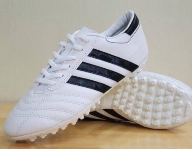 Một đôi giày đá bóng giá rẻ 100k trên sân cỏ nhân tạo, tượng trưng cho lựa chọn tiết kiệm của người chơi