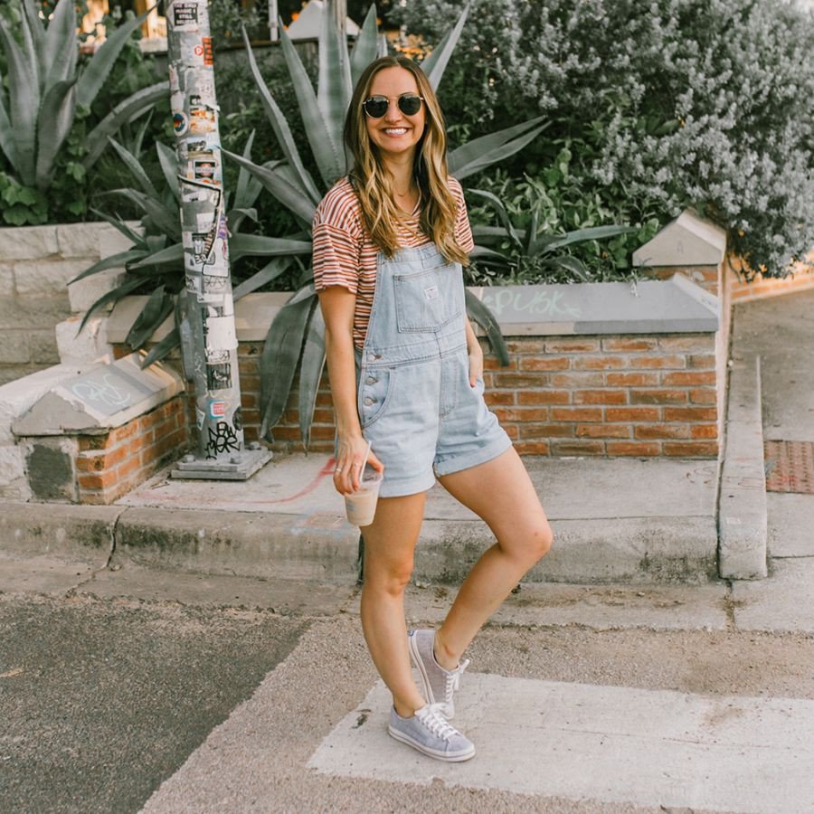 Cô gái mặc váy yếm denim với áo phông trắng kết hợp giày thể thao đen trắng, tạo phong cách năng động và trẻ trung