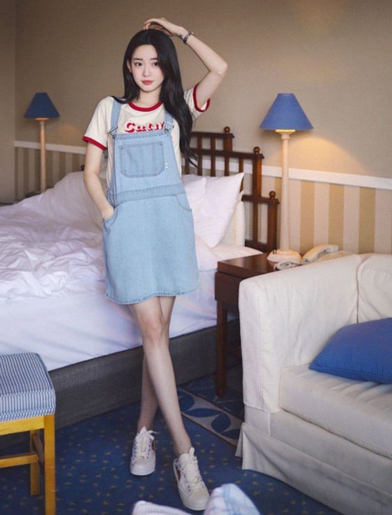 Cô gái mặc váy yếm jean dài và áo phông trắng, phối cùng giày thể thao