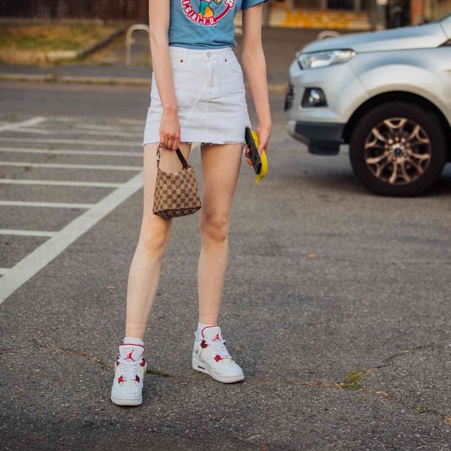 Một cô gái tạo dáng với váy ngắn màu đen và giày sneaker trắng, thể hiện sự năng động của phong cách giày thể thao mặc váy