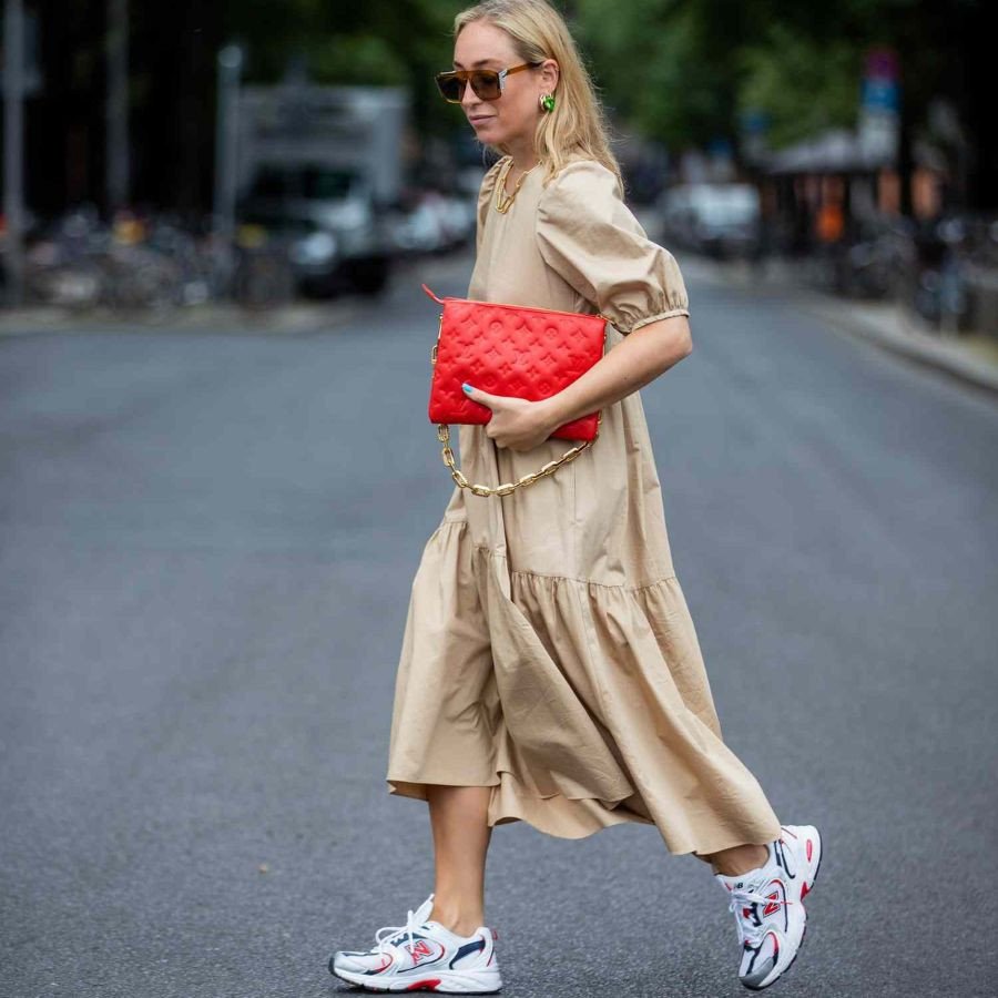 Một cô gái thể hiện sự tự tin và phong cách với giày thể thao mặc váy, tay cầm túi xách màu trắng