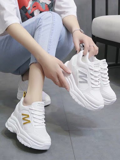 Một cô gái với đôi giày thể thao đế độn màu kem đang bước đi trên đường, thể hiện phong cách thời trang cá tính