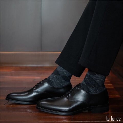 Người đàn ông mặc suit xanh đậm đang ngồi, với đôi giày tây màu nâu và vớ màu xanh navy sọc nhỏ