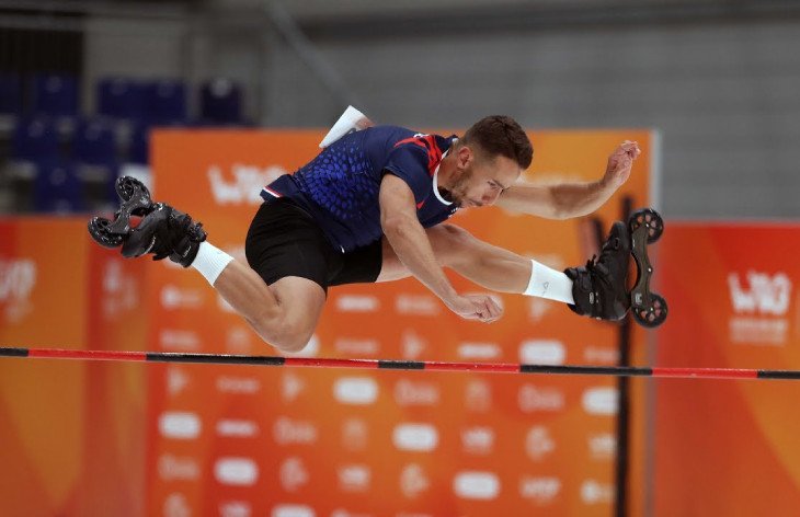 Người trượt patin thực hiện pha nhảy cao (High Jump) qua một thanh xà, thể hiện sức bật và kỹ thuật tiếp đất